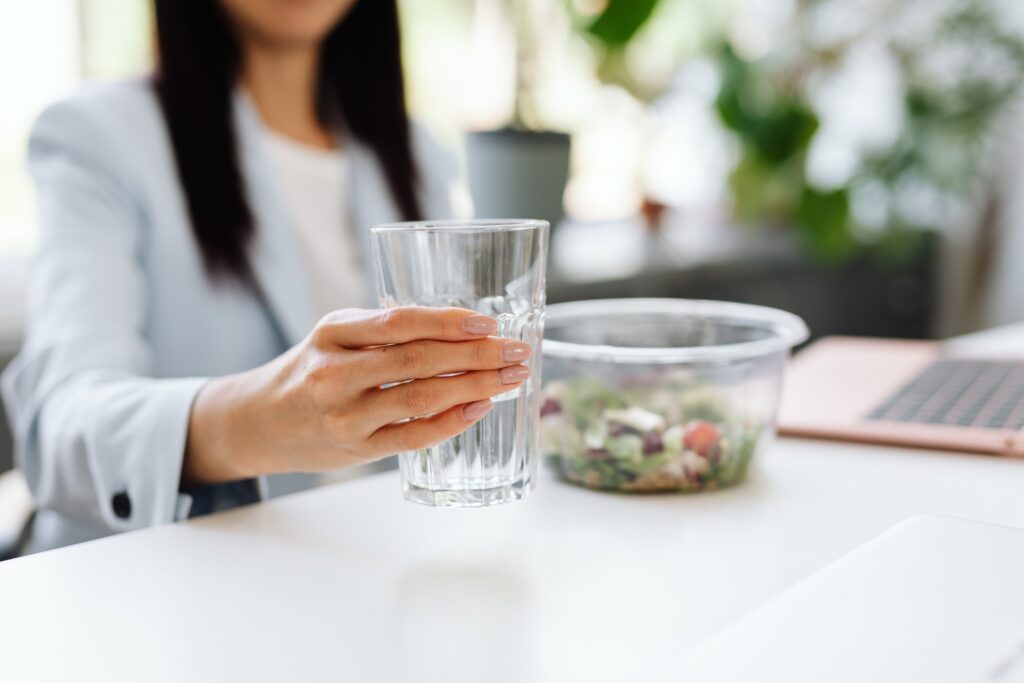 A woman in a business setting holding a glass of water with salad nearby.